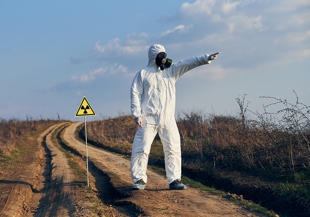 man protective coverall gas mask standing village road field caution sign